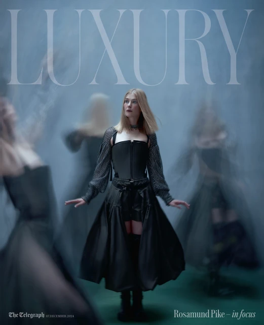 Rosamund Pike in a fashion editorial featuring a woman in a black outfit with layered skirts and sheer sleeves posing in a smoky setting.