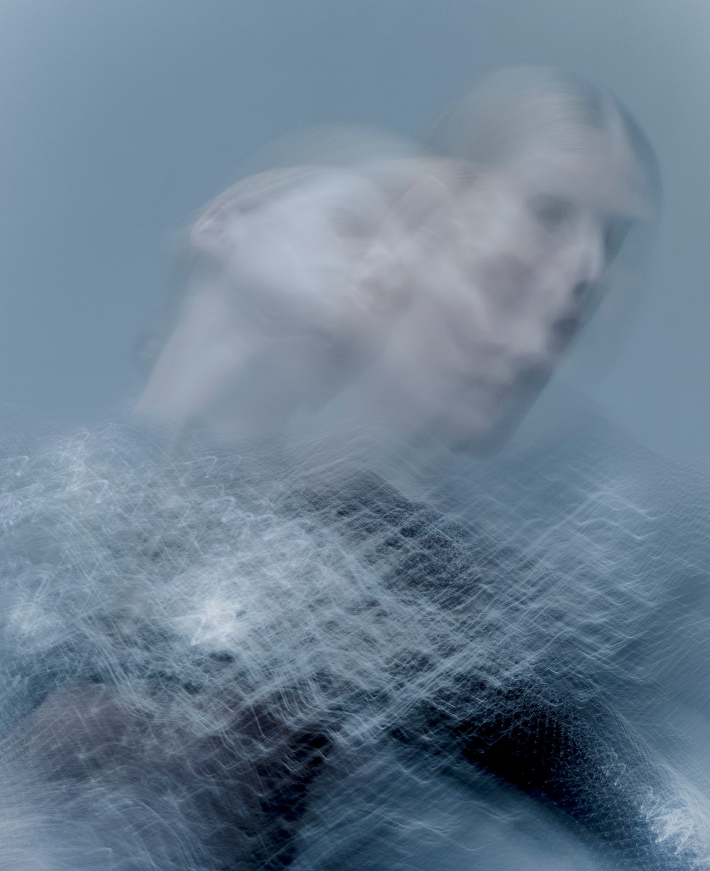 Abstract motion blur portrait of a female with a light blue background, showing a semi-transparent figure in dynamic movement.