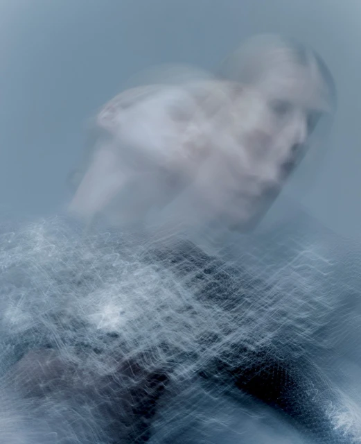 Abstract motion blur portrait of a female with a light blue background, showing a semi-transparent figure in dynamic movement.