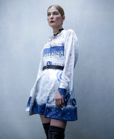 Woman in literary-themed dress with black belt and thigh-high boots poses indoors with a smooth gradient studio background.