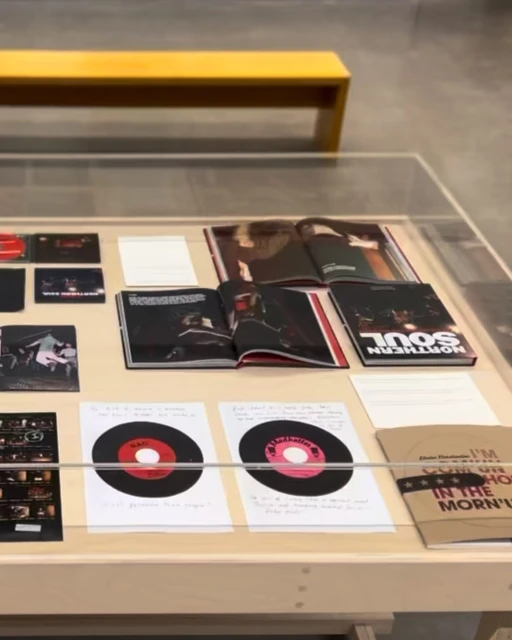 Close-up of a table with magazines, records, and promotional materials; natural indoor lighting; muted color palette with neutral tones.