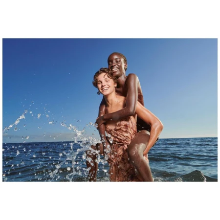 Two women smiling and wading in the ocean under a bright blue sky with splashing water around them on a sunny day.