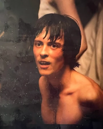 Portrait of a man with dark wet hair looking upwards with an open expression, captured with heavy grain.