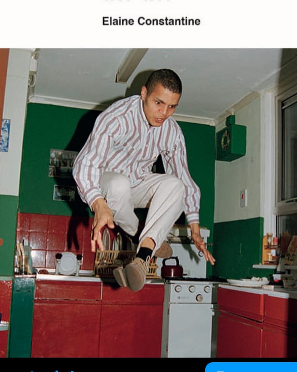 Adult male jumps over red and white kitchen stove in green kitchen under fluorescent lighting, showcasing indoor activity and home environment.