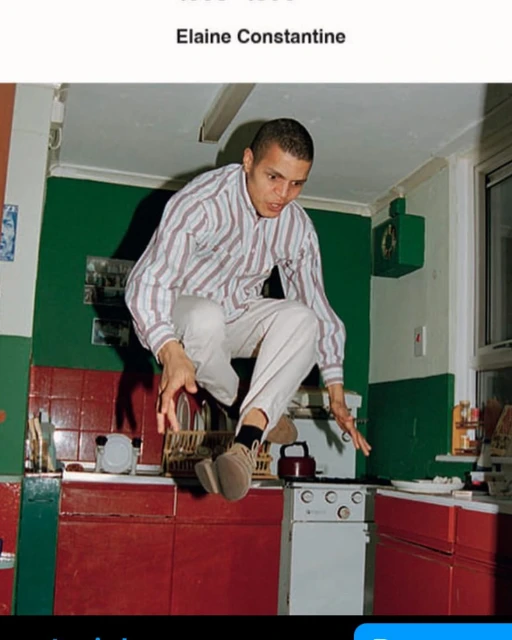 Adult male jumps over red and white kitchen stove in green kitchen under fluorescent lighting, showcasing indoor activity and home environment.
