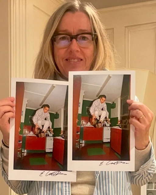 Woman holding two identical photographs indoors. The photos show a person sitting on a red kitchen counter.