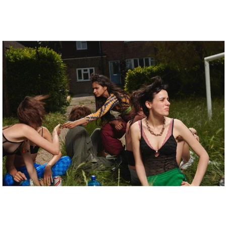 Group of young adults relaxing outdoors in tall grass outside a brick residential building photographed by Elaine Constantine