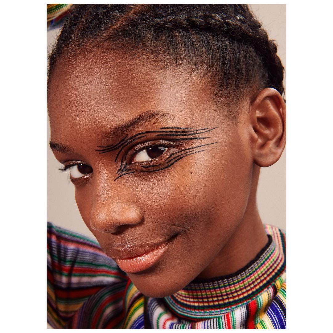 Close-up of a woman with braided hair and creative graphic black eyeliner, wearing a striped top, beauty and fashion concept.