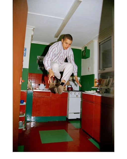 Young adult male in a striped shirt mid-air jump in a retro-style kitchen with red and green accents, creating a dynamic and whimsical scene.