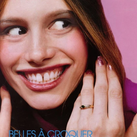 Close-up of a smiling young woman with auburn hair, pink glitter nails, and a ring on her finger, against a pink background.