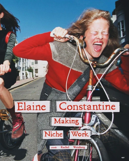 Two women riding bicycles on a city street, one with a very expressive face, wearing a red sweater with gray accents.