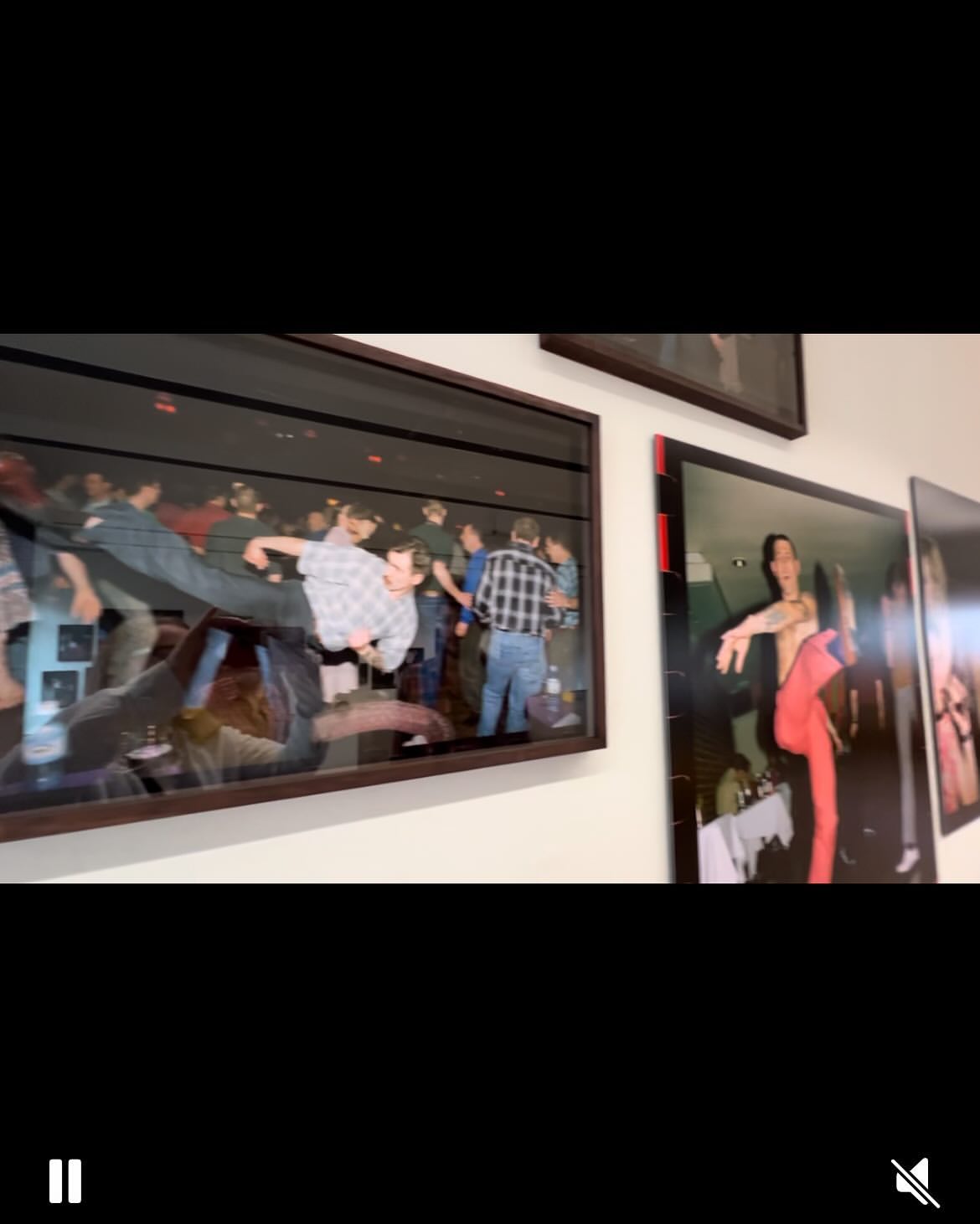 Framed photographs hang on a wall in a gallery setting, capturing images of people at an event and a dancer in motion.