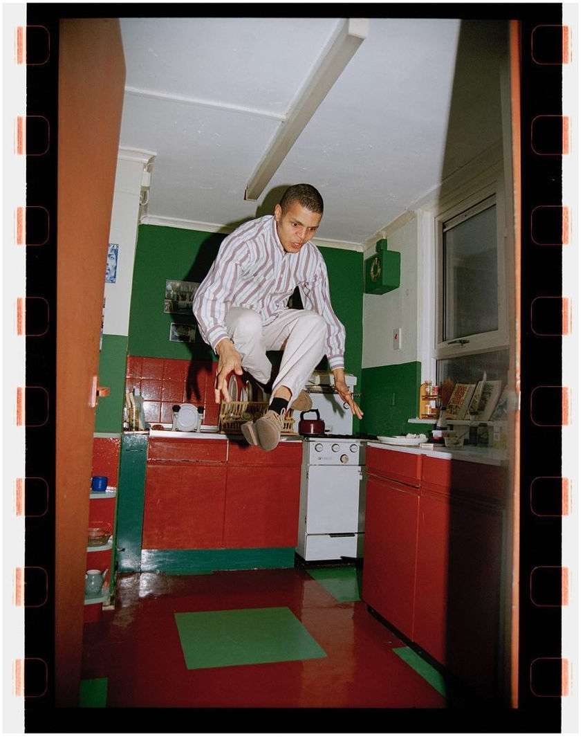 Man jumping in a retro kitchen with red cabinets and green accents, captured with vintage film aesthetic and a full-frame shot.