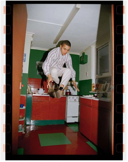Man jumping in a retro kitchen with red cabinets and green accents, captured with vintage film aesthetic and a full-frame shot.