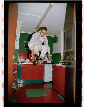 Man jumping in a retro kitchen with red cabinets and green accents, captured with vintage film aesthetic and a full-frame shot.