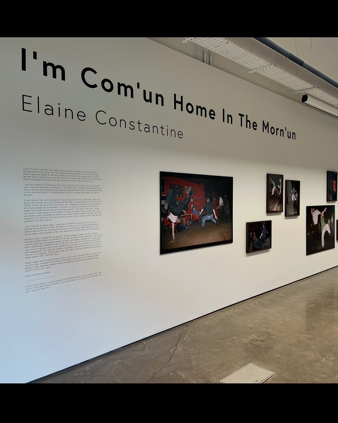 Bright and spacious art gallery featuring framed photographs on white walls, complemented by visible text about the artist and exhibition.