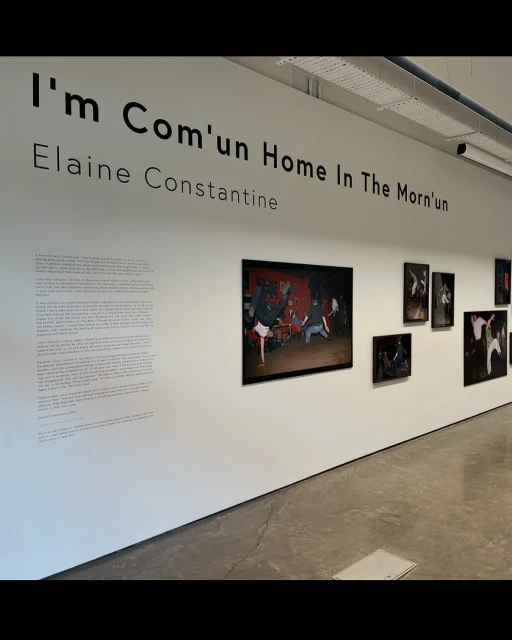 Bright and spacious art gallery featuring framed photographs on white walls, complemented by visible text about the artist and exhibition.