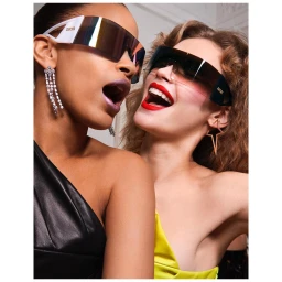 Two women wearing futuristic shield sunglasses and statement earrings laughing together in a close-up portrait by Elaine Constantine.