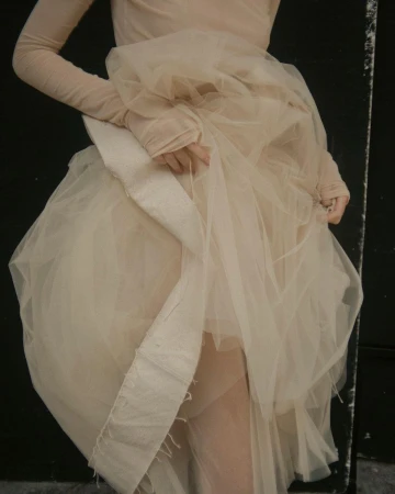 Close-up of a person wearing a pale nude tulle dress with layered sheer fabric and a structured cream panel.