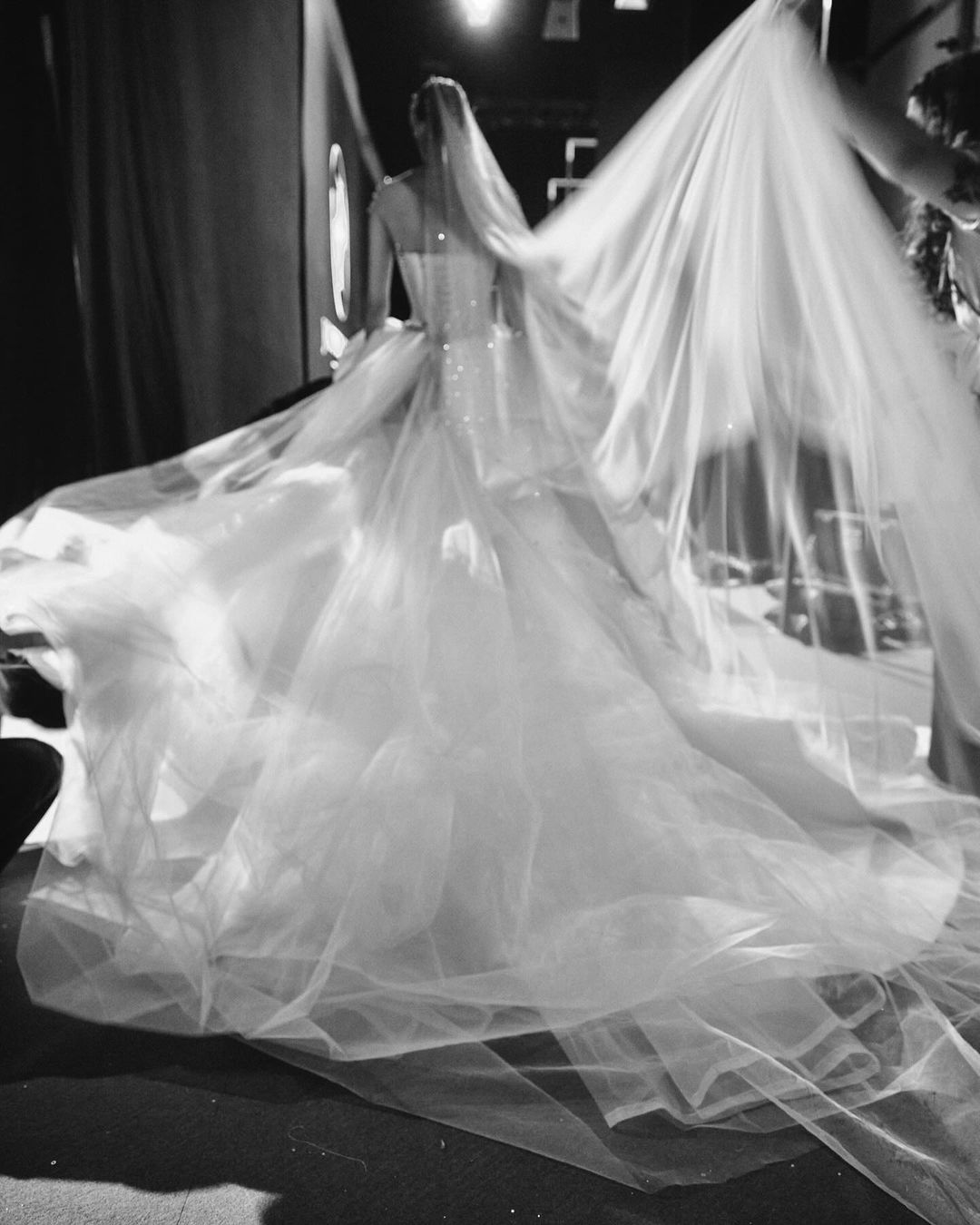 Back view of woman in elegant, voluminous white wedding dress and veil. Soft lighting, fashion, black and white.
