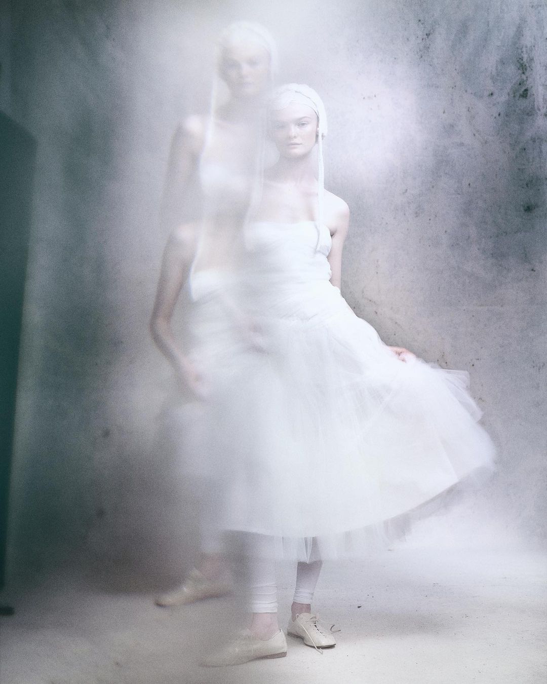 Woman in white dress with ethereal layered effect, posing against a textured background, creating a dreamy and artistic fashion image.