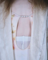 Close-up of a person wearing a beige textured outer garment over a patterned garment with a pearl-beaded strap detail.