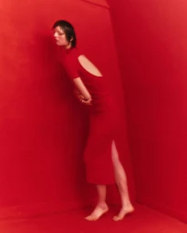 Woman in a red backless midi dress leaning against a vibrant red wall