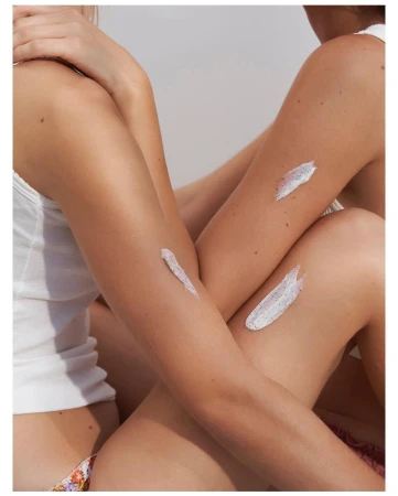 Close-up portrait of two women wearing white tank tops with exfoliating cream smeared on their arms, photographed by Eleonore Wismes