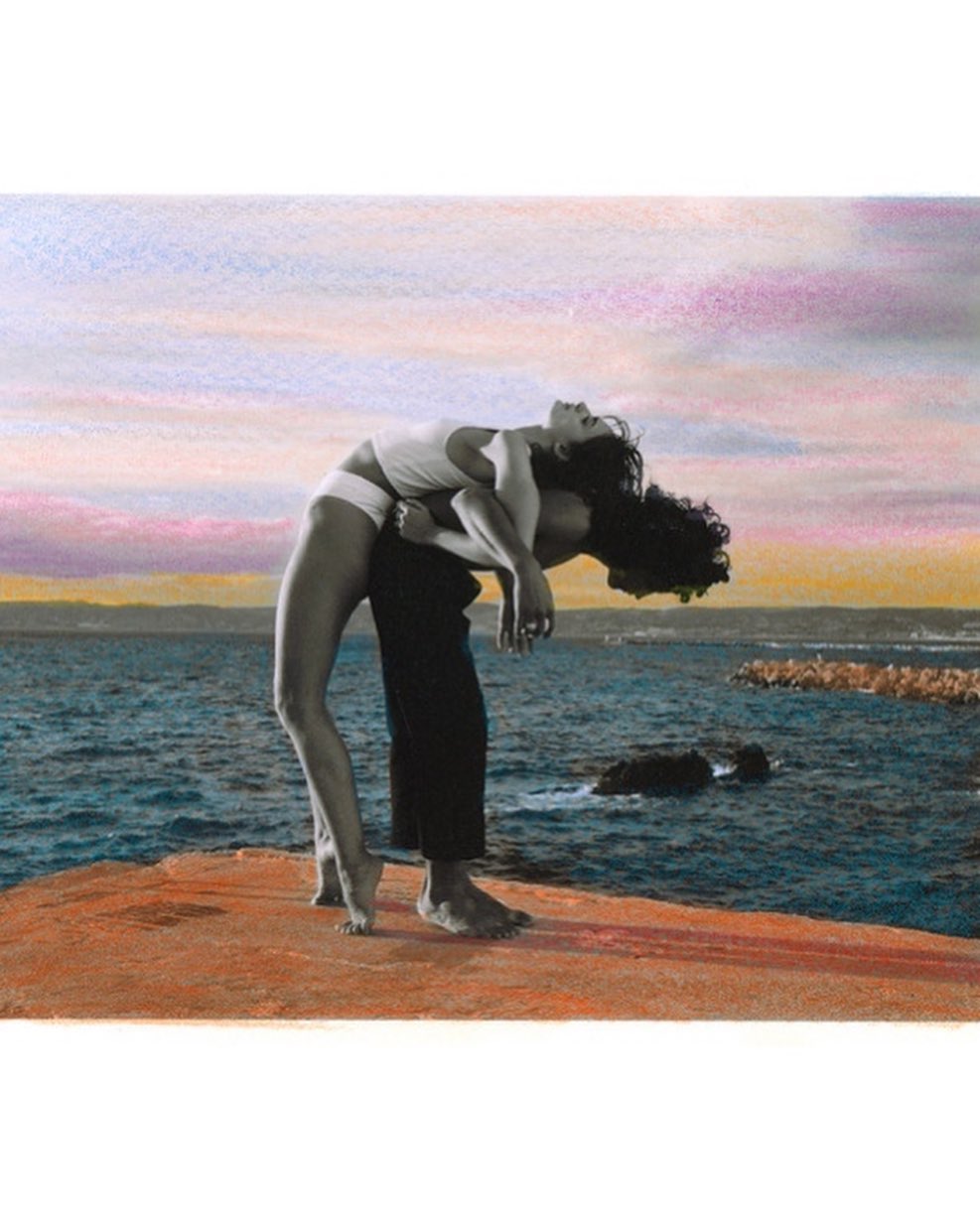 Couple posing together on rocky beach with a view of the ocean and colorful sky, capturing a moment of connection in a seaside setting.