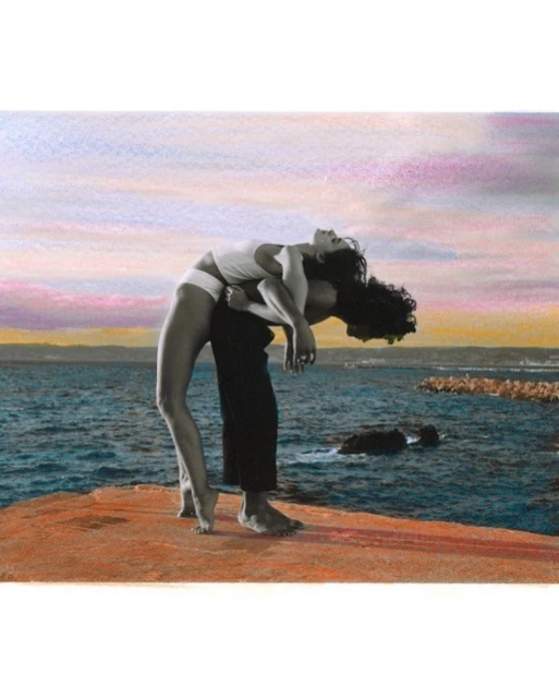 Couple posing together on rocky beach with a view of the ocean and colorful sky, capturing a moment of connection in a seaside setting.