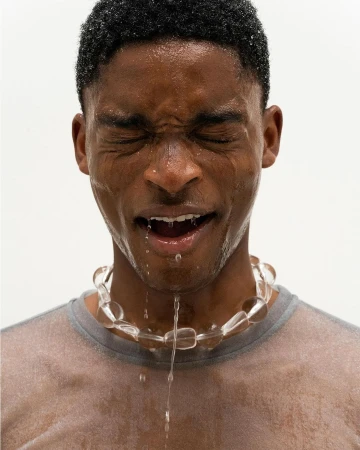 Close-up of a wet black man wearing a translucent t shirt and beaded necklace with his eyes closed in Paris
