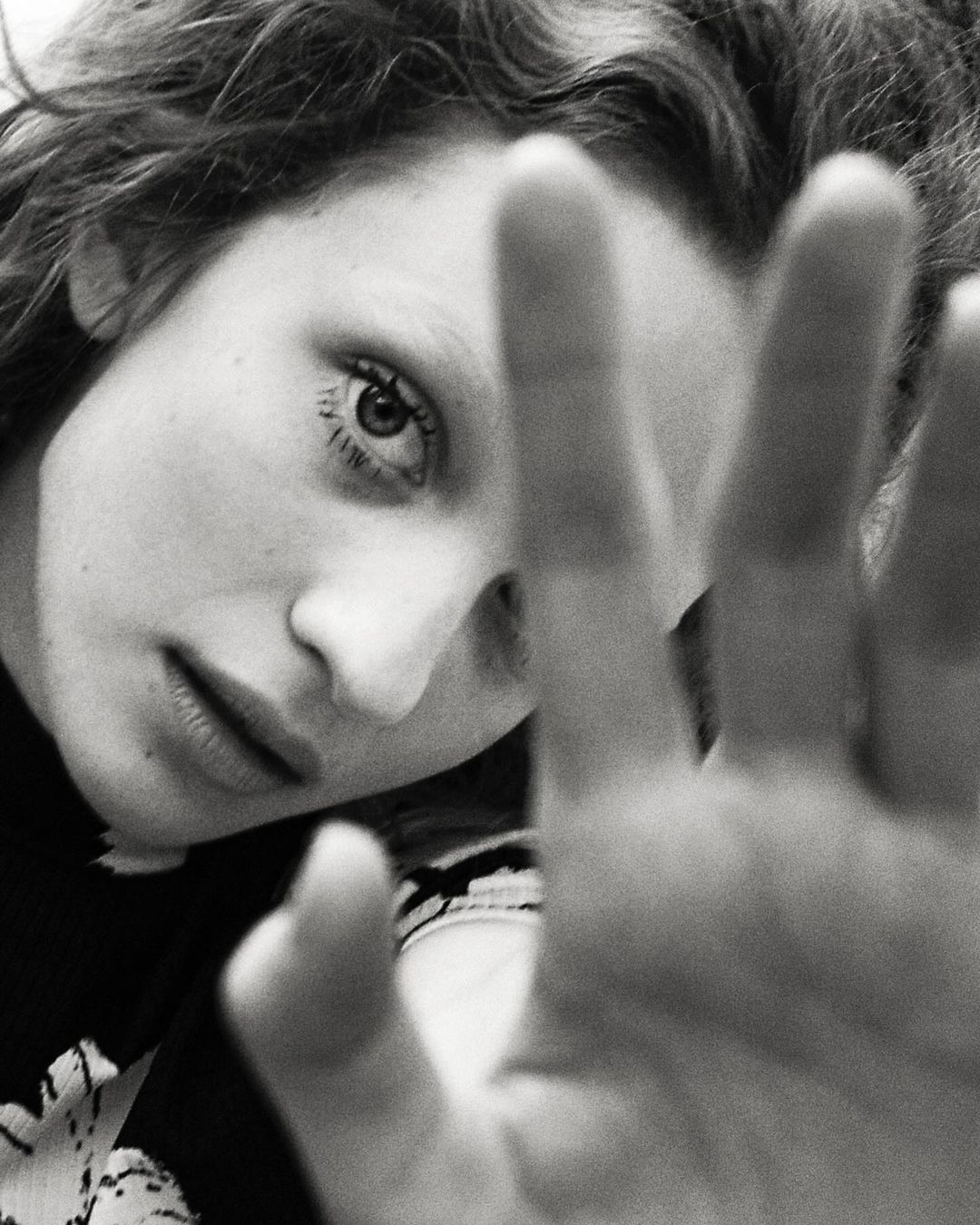 Close-up black and white portrait of a woman with her hand raised in the foreground, shot in Paris by Eleonore Wismes.