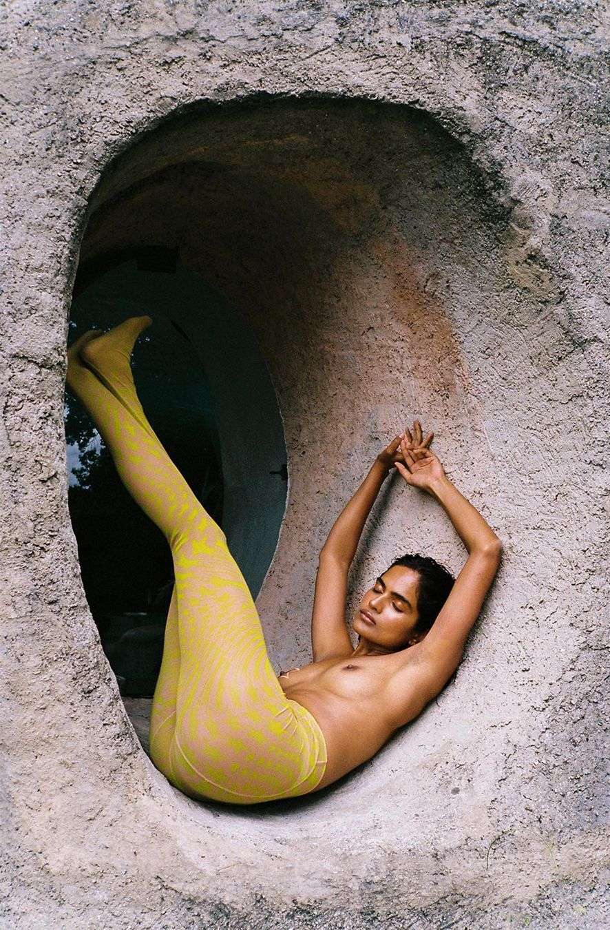 Woman in yellow tights poses inside a concrete tunnel, arms overhead. She looks relaxed, bathed in soft natural light.