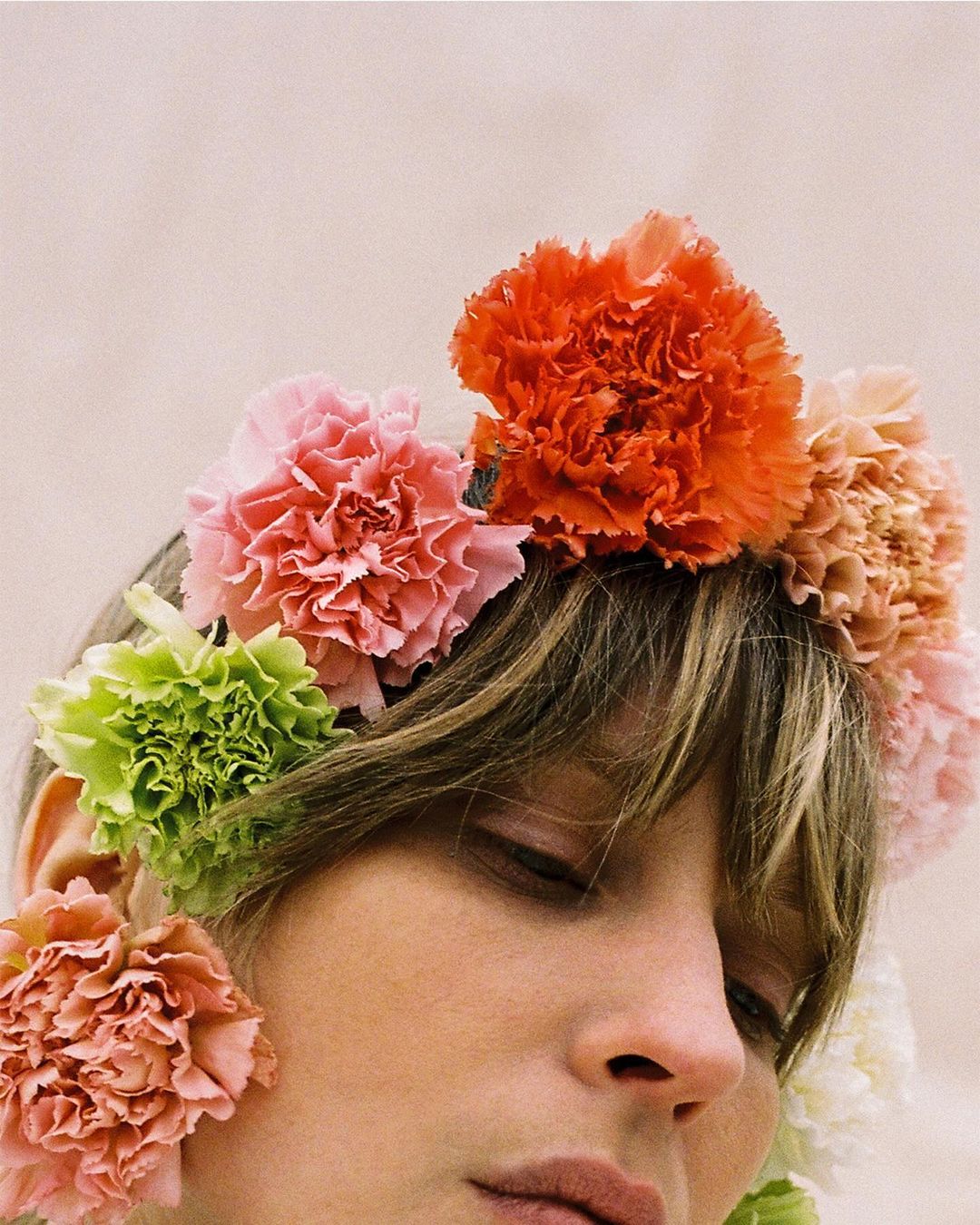 Close-up portrait of a young woman adorned with a colorful flower crown, eyes closed, soft lighting, and a neutral background. Beauty shot.
