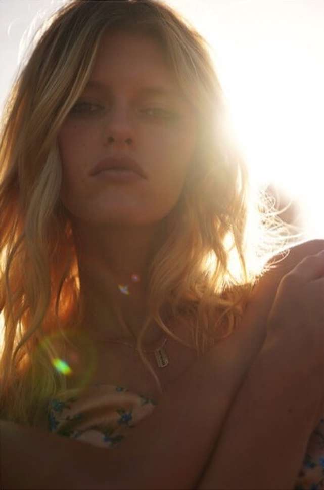 Close-up portrait of a blonde woman in sunlight, featuring soft focus, natural light, and a light floral top.