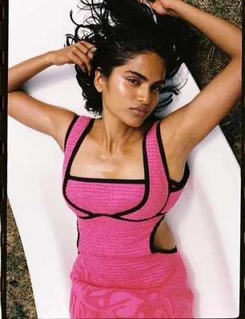 Woman with dark hair lying on a white surface wearing a pink dress with black trim, captured in an eye-level shot.