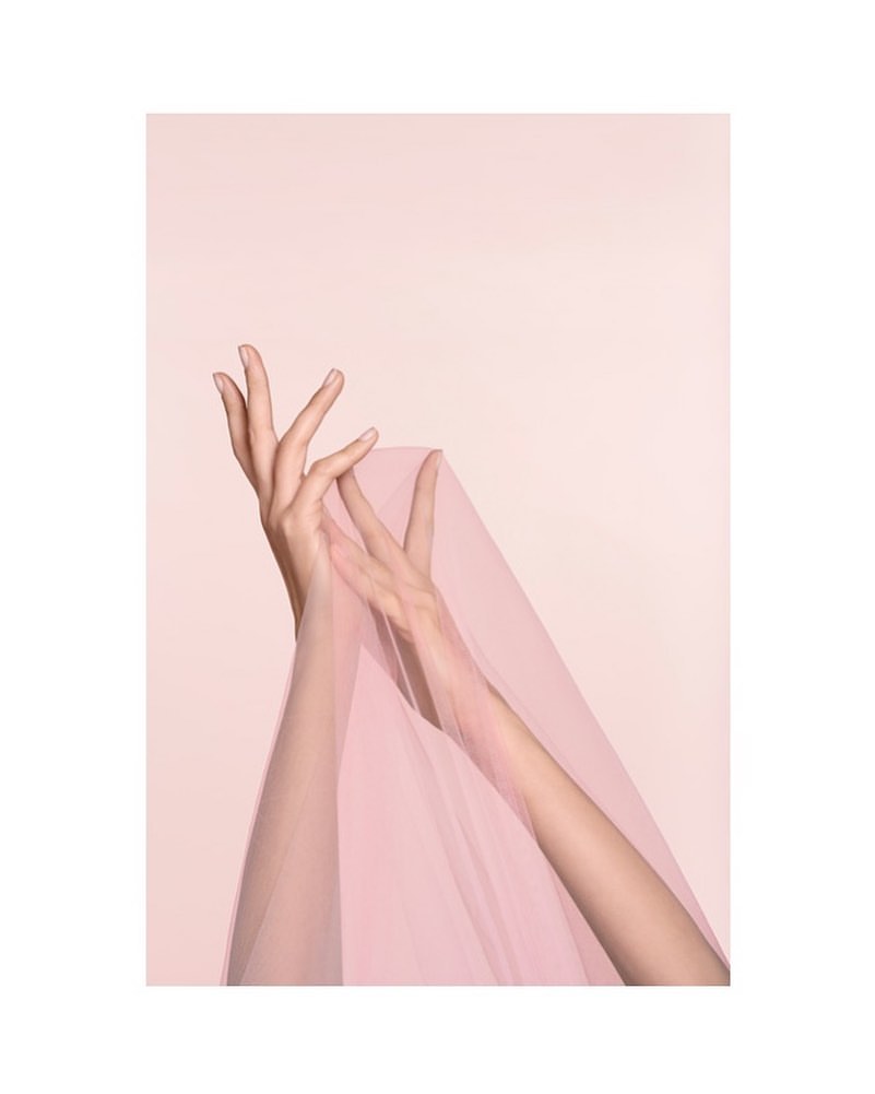 Elegant image featuring a woman's hands gracefully posed, holding a sheer pink veil against a soft pastel background, creating a serene beauty shot.