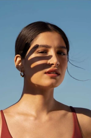 Close-up portrait of a woman outdoors with a hand casting a shadow across her face against a clear blue sky background.