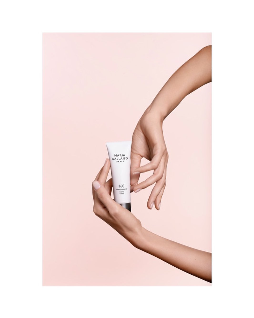 Hands holding a white tube of Maria Galland H2O moisturizing cream against a soft pink background in a beauty product shot.