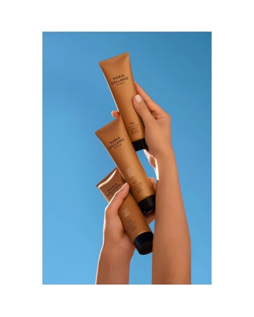 Trio of tanning lotion tubes with black lids held by light-skinned woman's hands against a bright blue sky background in studio shot.
