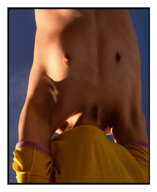 Artistic close-up shot of a shirtless person against a blue sky, capturing the play of light and shadow on their upper body.