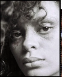 Close-up black and white portrait of a person with curly hair and visible freckles photographed by Eleonore Wismes.
