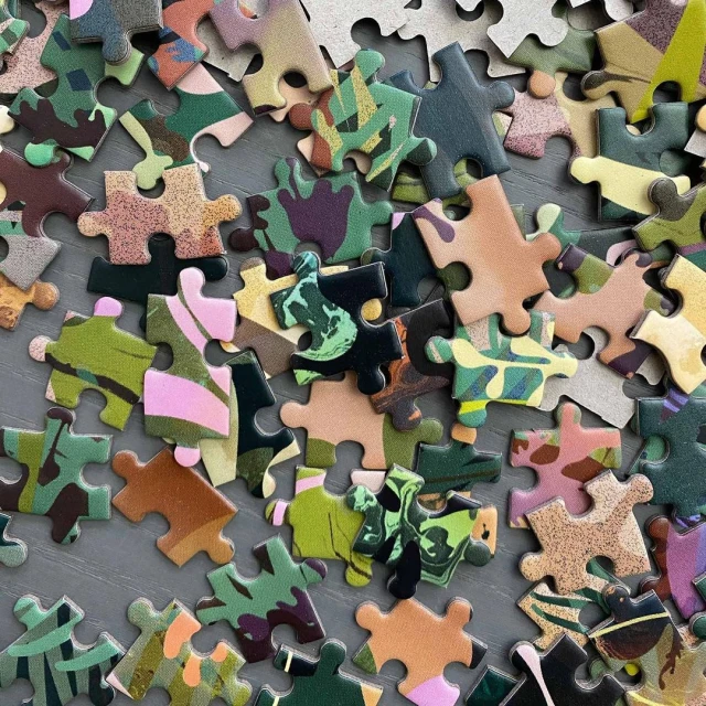 Close-up of a high-angle shot features puzzle pieces with camouflage patterns scattered across a gray surface, creating a textured abstract.