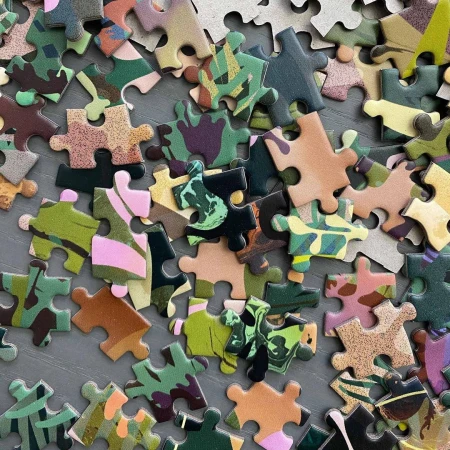 Close-up of a high-angle shot features puzzle pieces with camouflage patterns scattered across a gray surface, creating a textured abstract.