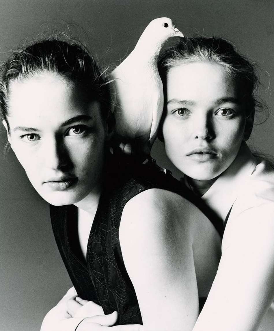 Two women pose in a black and white portrait with a white dove perched on the shoulder of one, creating a classic, intimate image.