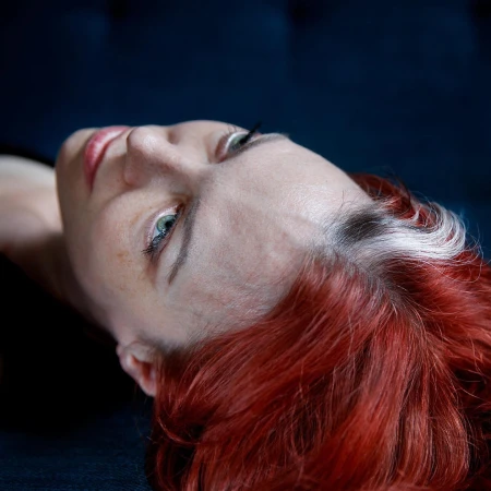 Close-up portrait of a woman with red hair and a white streak, captured from an overhead angle by Elinor Carucci.