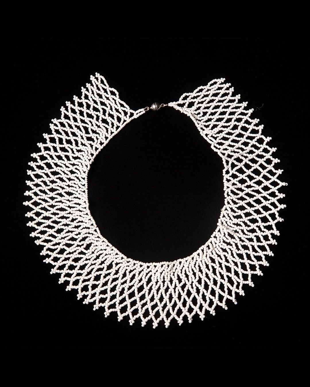 Elegant white beaded necklace in a net-like design against a stark black background, showcasing intricate craftsmanship and texture.