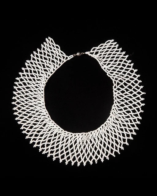 Elegant white beaded necklace in a net-like design against a stark black background, showcasing intricate craftsmanship and texture.