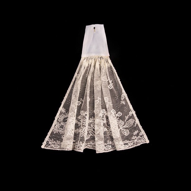 Lace textile with floral pattern and white fabric hanging loop against a stark black background, creating contrast in texture and color.