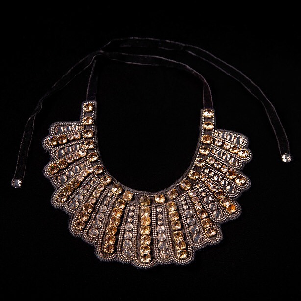 Close-up studio shot of an ornate statement necklace with amber and clear gems on a black velvet tie against a dark background.